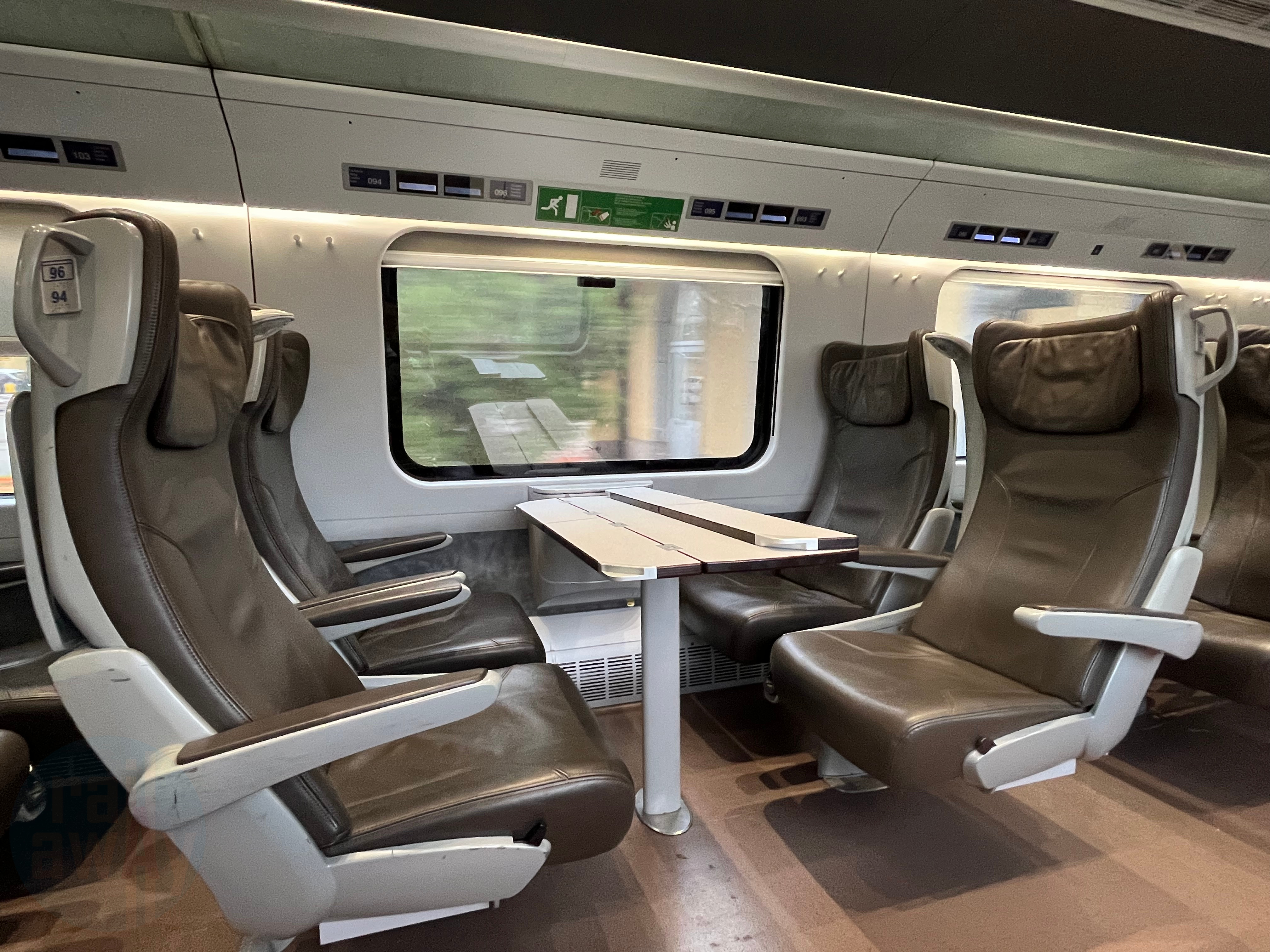 Four brown leather seats around a table in First Class with a window and foldable table