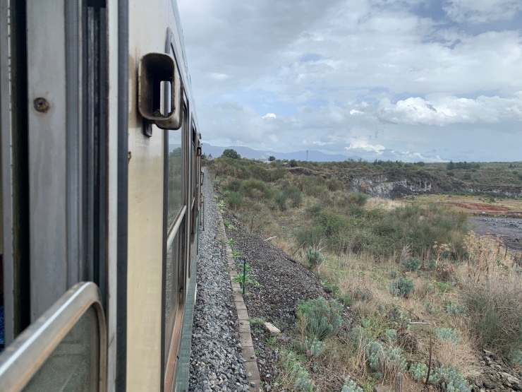 A view out of the window of the train with volcanic lava fields on the right and the side of the train's exterior on the left.